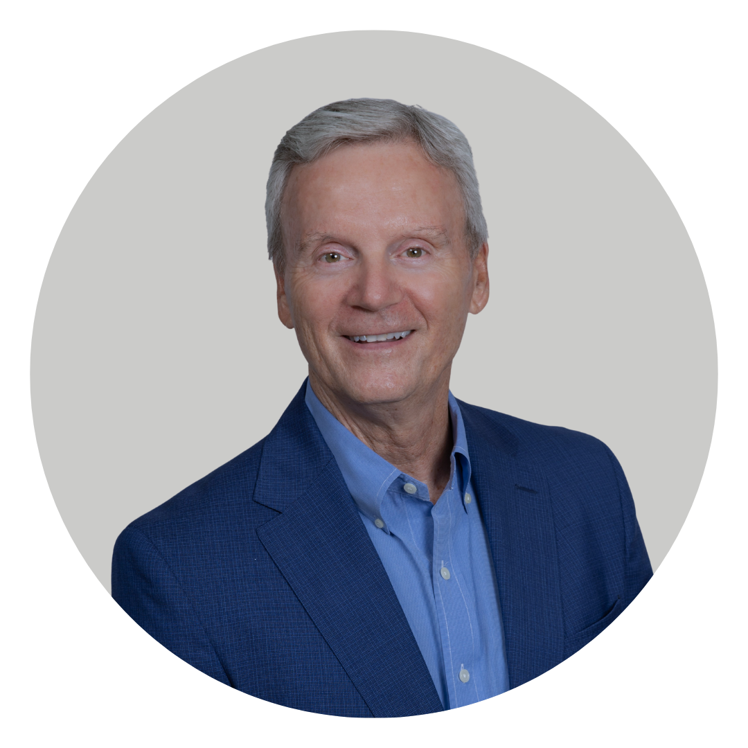 A man with gray hair, wearing a blue blazer and light blue shirt, smiling against a gray background in a circular frame.