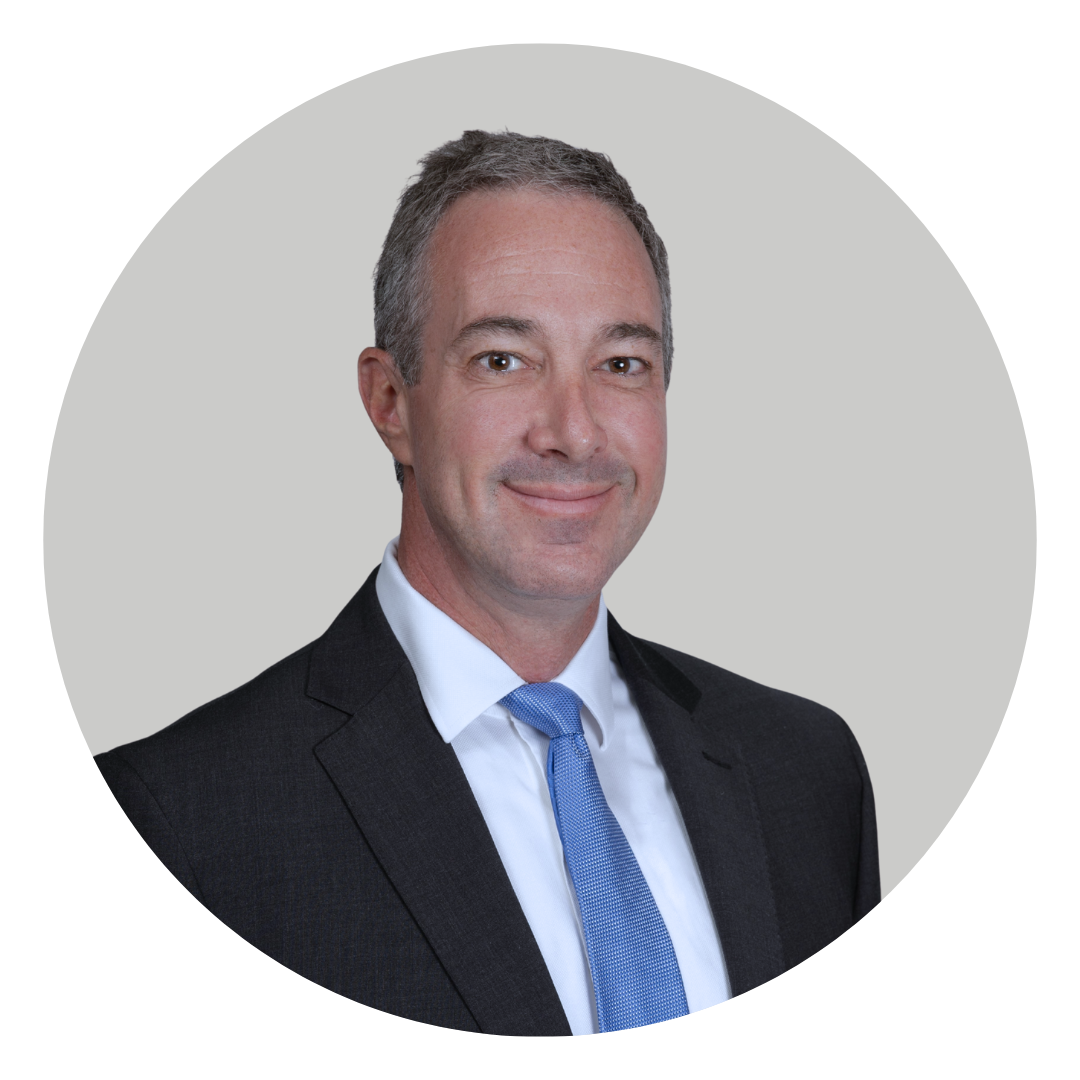 A professional headshot of a man wearing a dark suit and a light blue tie, smiling against a light gray circular background.