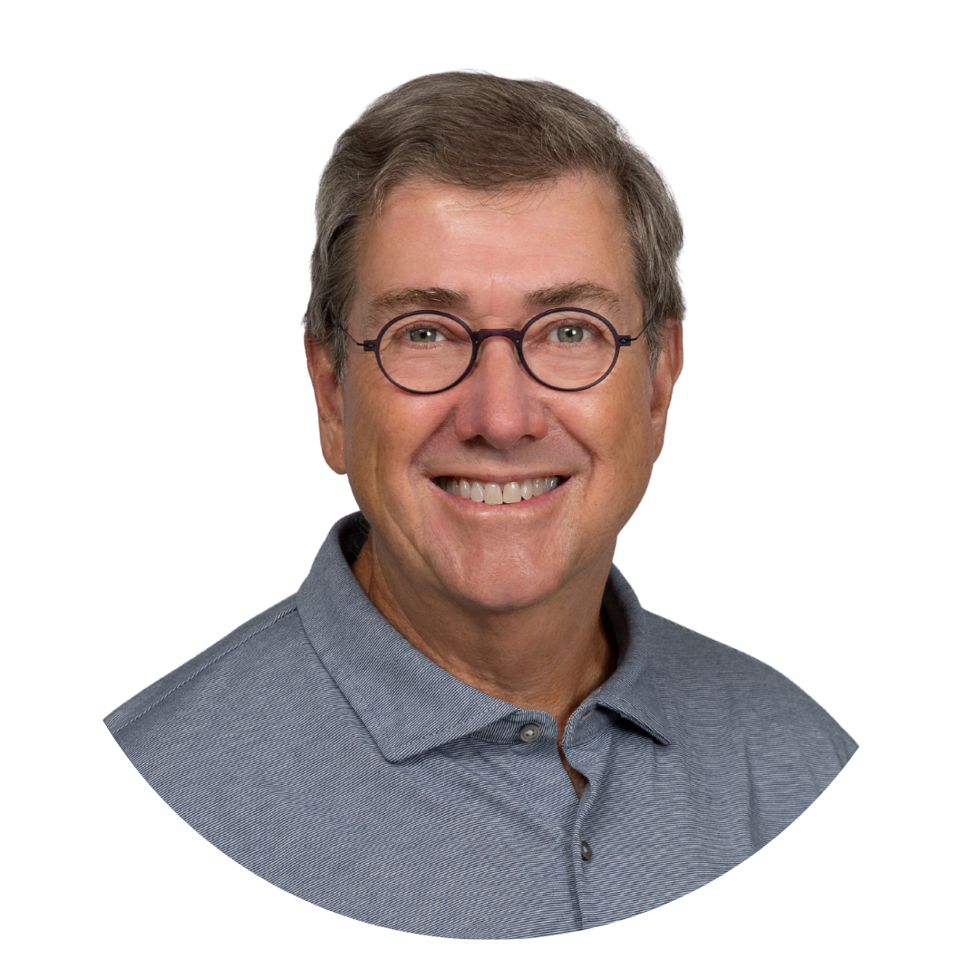 A smiling middle-aged man wearing glasses and a gray collared shirt, set against a plain white background. His hair is gray and slightly tousled.