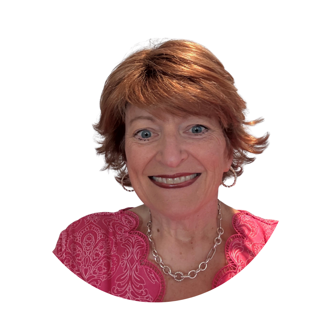 A woman with short, wavy reddish-brown hair smiling directly at the camera. She is wearing a pink shirt with intricate patterns and a silver chain necklace. The background is white, creating a clear focus on her face.