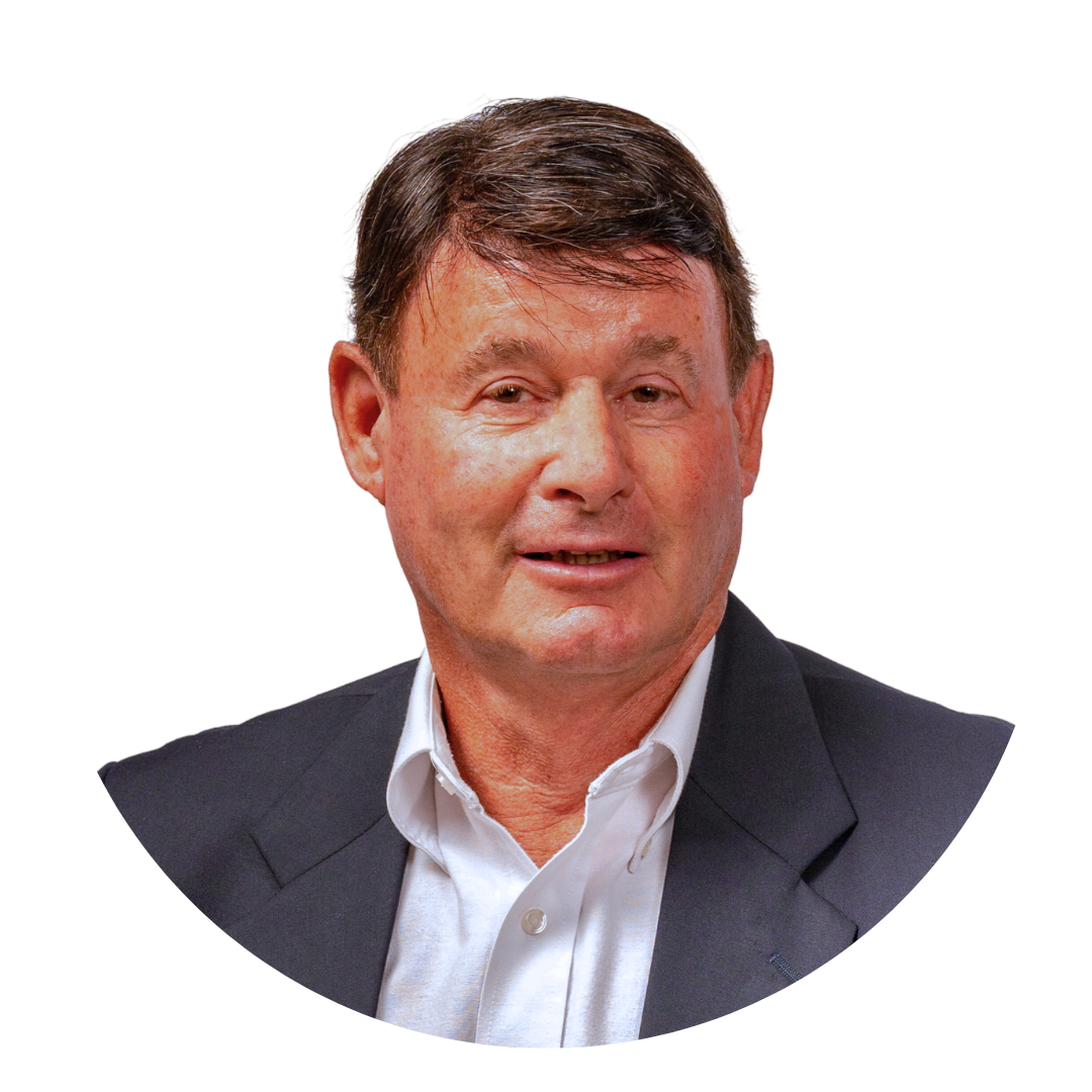 A man with short dark hair, wearing a light blue shirt and dark blazer, is smiling while facing the camera. The background is plain white, and the image is framed in a circular shape.