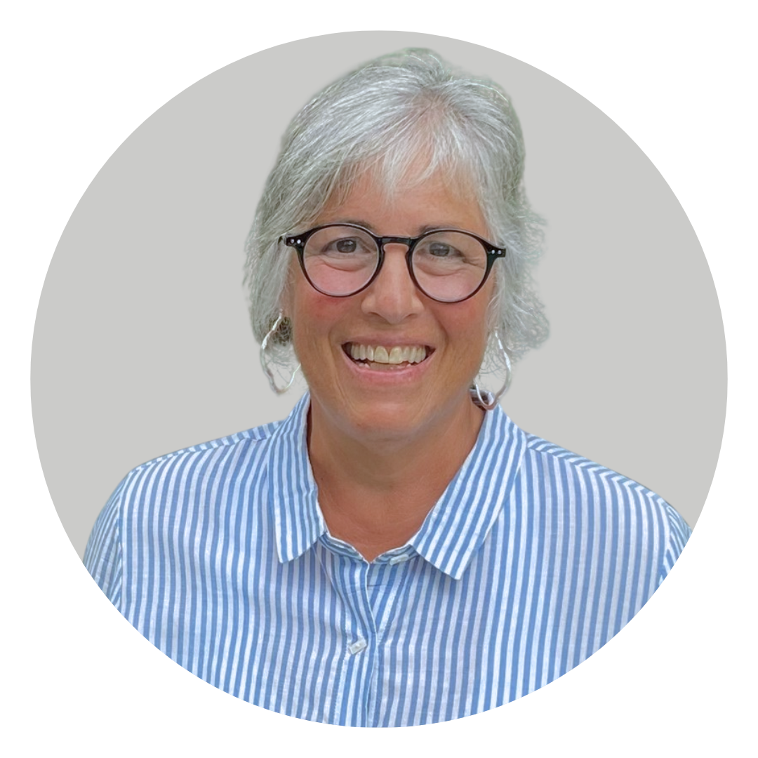 A smiling woman with short gray hair, wearing glasses and a blue and white striped shirt, poses against a light gray circular background.