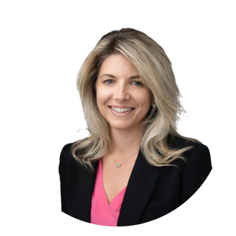 A professional headshot of a woman with long, wavy blonde hair, wearing a black blazer over a pink blouse. She is smiling against a plain white background.