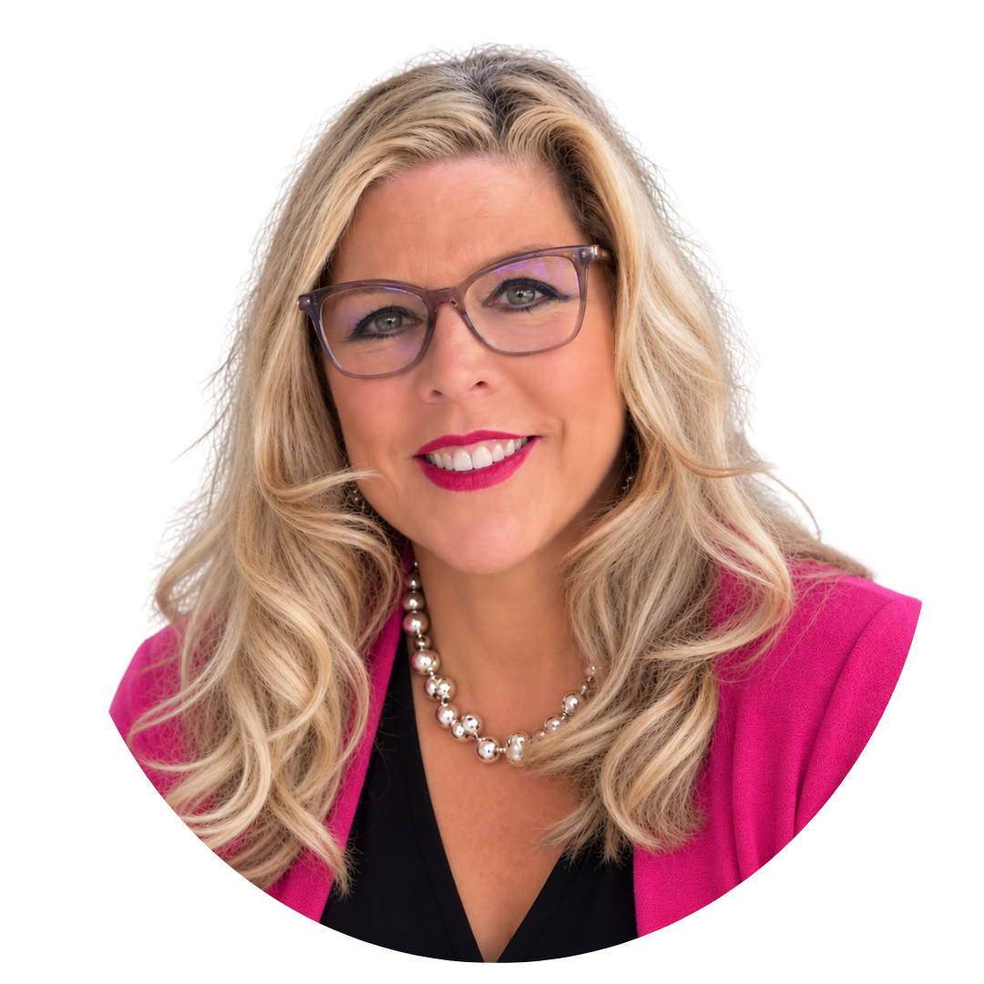 A woman with blonde hair and purple glasses wears a bright pink blazer and pearl necklace against a plain white background.